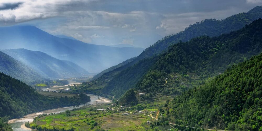 Valley in Bhutan near Punakha with rice fields and typical houses. Travel to Bhutan and enjoy the beautiful landscape of farms and mountains in this buddhist country.